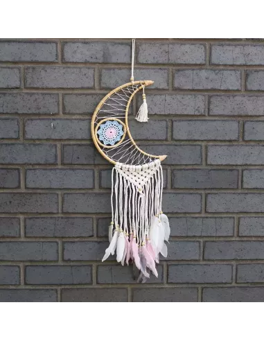 atrapasueños con forma de luna y plumas colgando sobre un fondo de ladrillos grises