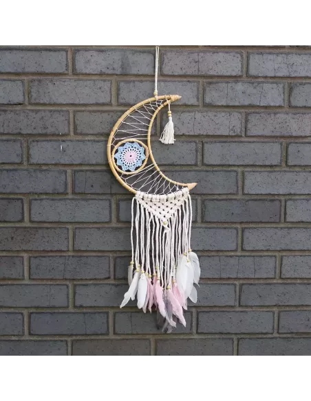atrapasueños con forma de luna y plumas colgando sobre un fondo de ladrillos grises