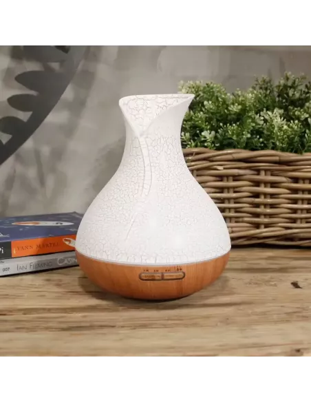 Difusor de aromas color nácar con base de madera y forma de jarrón con cambio de color y temporizador sobre un mueble de madera